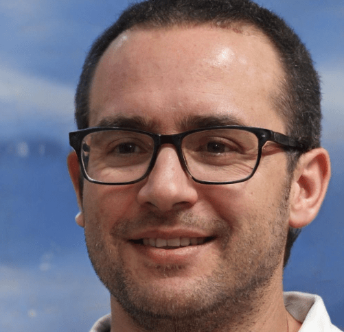 A man with short dark hair, glasses, and light stubble smiles gently. He is wearing a white shirt, and the background appears to be a painted blue scene with subtle hints of clouds. In his other hand, he holds a toolkit for electric gate repairs.